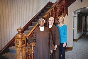 Sr. Immaculata Osterhaus and Sr. Maria Goretti Ifeorah, Carmelite Sisters of the Divine Heart of Jesus, and Denise Bates, director of the Carmelite Home for Boys, stand by the staircase the order’s foundress, Mother Maria Theresa of St. Joseph, saw in a vision when she was seeking a place to relocate the home in 1916. Sr. Immaculata is superior of the order’s Northern Province; Sr. Maria Goretti is administrator of the home.