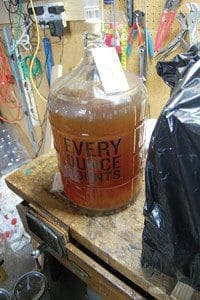 : The beer is stored in a large glass container that will be kept in a basement until it has finished fermenting. Above right: as Tim Logman looks on, Weingarten adds ingredients as part of the cooking process. (Catholic Herald photos by Ricardo Torres)