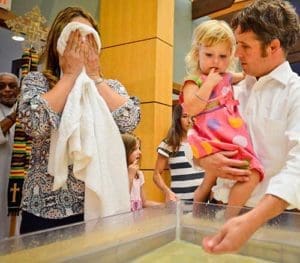 Mass of Peace attendees wash their hands and face in the baptismal font, at the invitation of Fr. Bob Stiefvater, who encouraged them to wash themselves in the waters of their baptism. Looking on is Luke Harrison, holding his daughter, Celia. The Mass of Peace at All Saints Church, Milwaukee, was held days after riots broke out in an area of the city following the killing by a Milwaukee police officer of an armed 23-year-old man after a traffic stop. (Catholic Herald photo by Juan C. Medina)