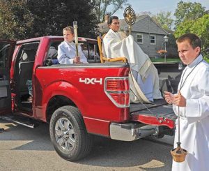Lumen Christi associate pastor Fr. Matthew Jacob, holding a monstrance with the Eucharist, rides in the back of a pickup truck during the six mile procession from the parish’s Thiensville site to its Mequon site.