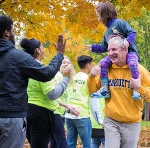 Riding the shoulders of her grandfather, Joe Hogan, Lilly Ibarra, a student at Catholic East Elementary School, Milwaukee, gives a high five to one of the volunteers along the route. (Catholic Herald photo by Peter Fenelon)