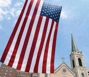 A 48-foot U.S. flag is seen June 24 outside Sacred Heart Church in downtown Peoria, Ill. In his Herald of Hope column, Archbishop Listecki suggests the church is under attack as a faith and a church by civil political forces. (CNS file photo/Tom Dermody, Catholic Post)