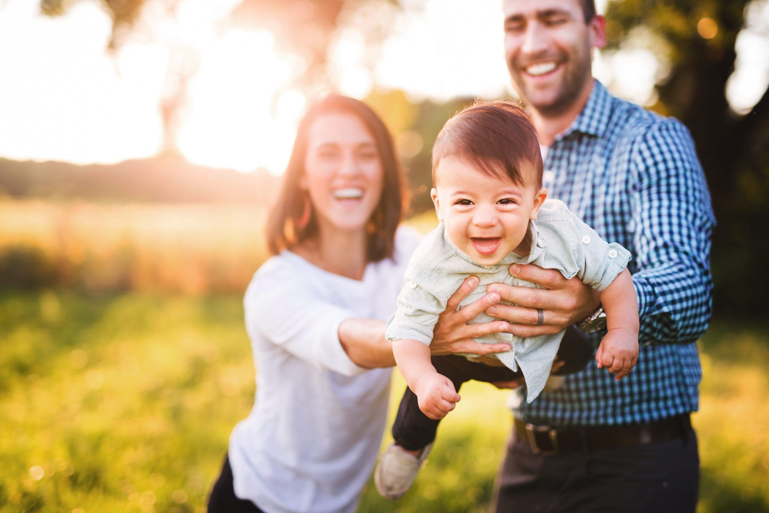 Portrait Of Cute Cheerful Baby Boy Playing With Parents In Park